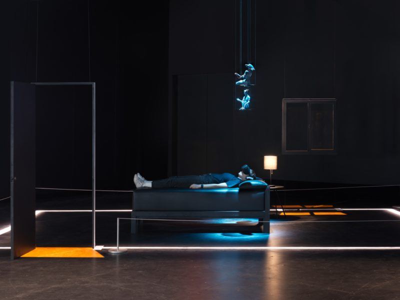 Morehshin Allahyari installation "She Who Sees The Unknown: Kabous," a person lying down on a bed with VR goggles on, and a sculpture hangs above them.