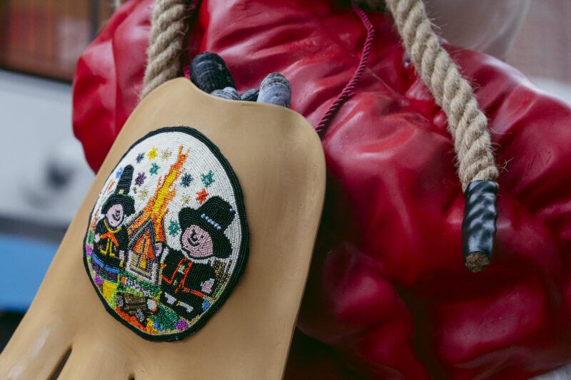Close-up of a glove with an embroidered patch depicting two cartoonish pilgrims and a campfire.
