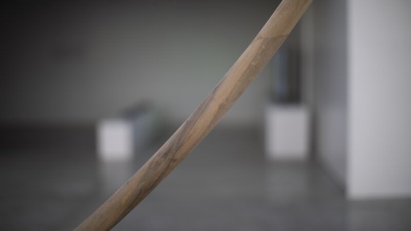 Detail of a curved sculpture in focus with a blurred, gallery space in the background.
