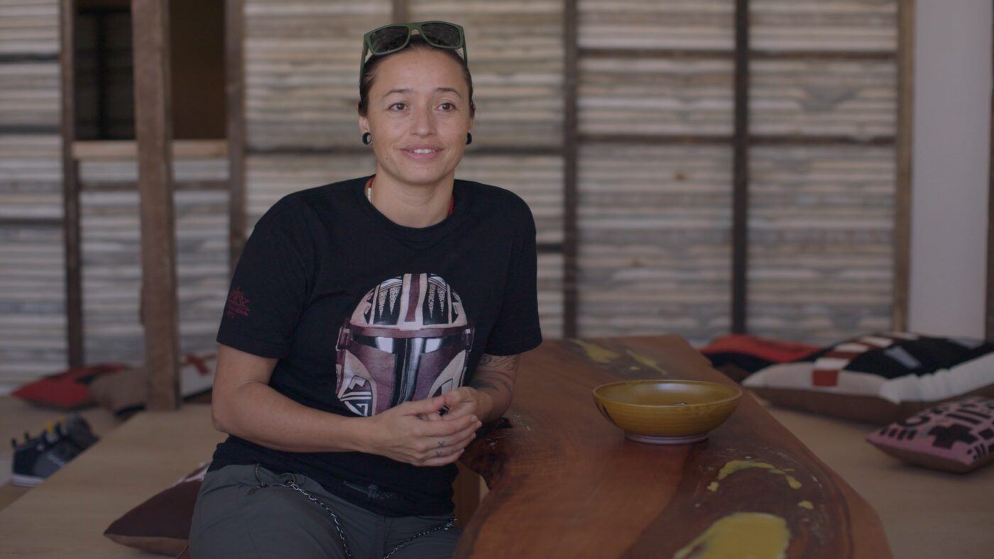 Rose B. Simpson hands clasped sitting in front of the wooden walls of her installation, "Dream House."