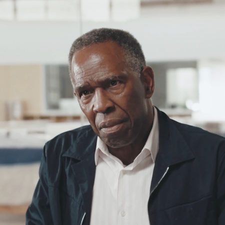 Charles Gaines looking intently at the camera, he wears a dark jacket over a white collared shirt.