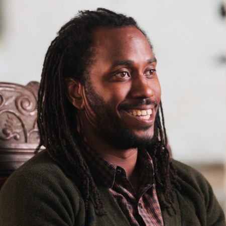 Side profile of Rashid Johnson sitting in a high back wooden chair.