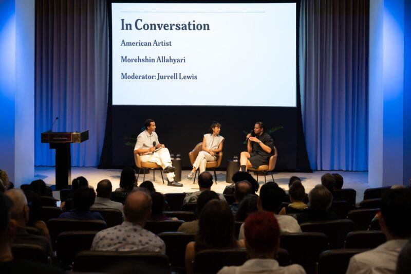 Three people sit on stage in a panel discussion titled "In Conversation" with American Artist, Morehshin Allahyari, and moderator Jurrell Lewis, in front of an audience and a large presentation screen.