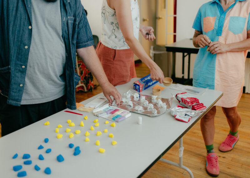 Three people stand around a table with colorful craft supplies and modeling clay.
